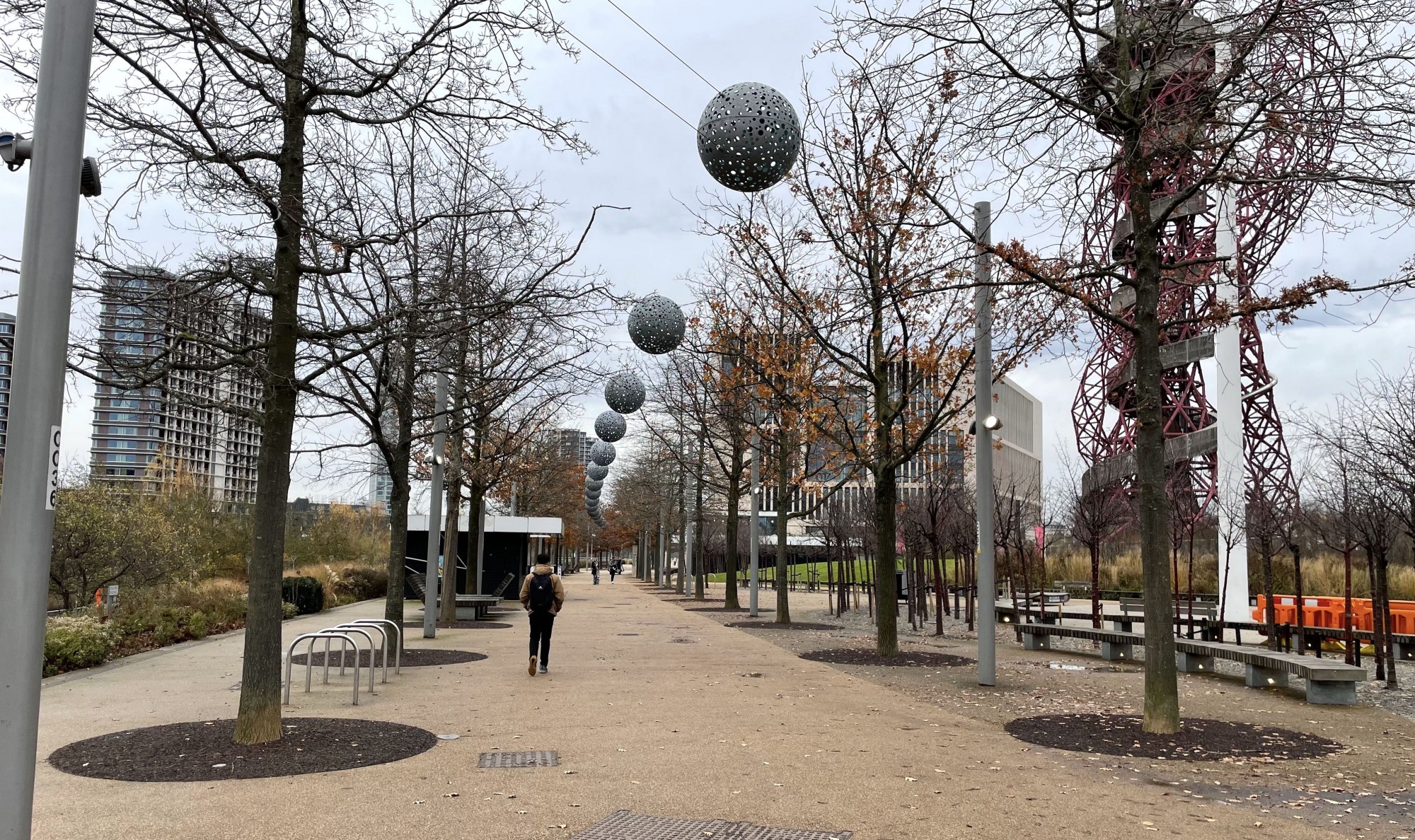 A person walking on a sidewalk with trees and balls from wires